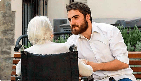 Voluntario de Hermanas Hospitalarias acompaña a una persona mayor en silla de ruedas